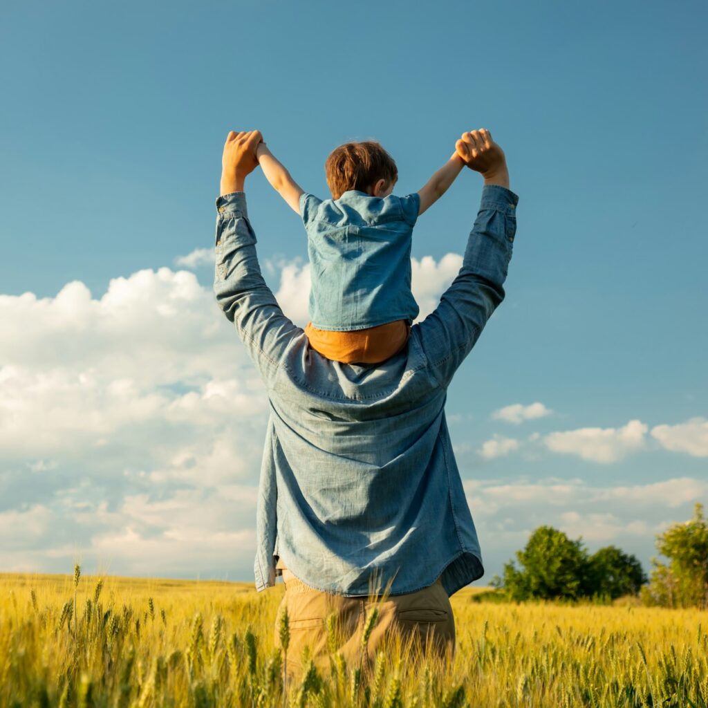 a man holding a child on his shoulders in a field
